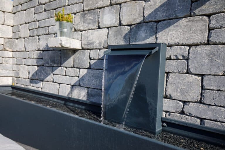 Moderne Wasserwand aus Metall mit rechteckigem Becken vor Betonsteinmauer als Wassergestaltung im Gartenbau in Wiesenttal von BELLA FLORA GmbH.