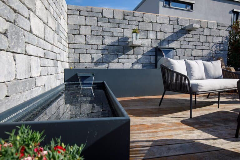 Moderne Wasserwand aus Metall mit rechteckigem Becken vor Betonsteinmauer als Wassergestaltung im Gartenbau in Buckenhofen von BELLA FLORA GmbH.