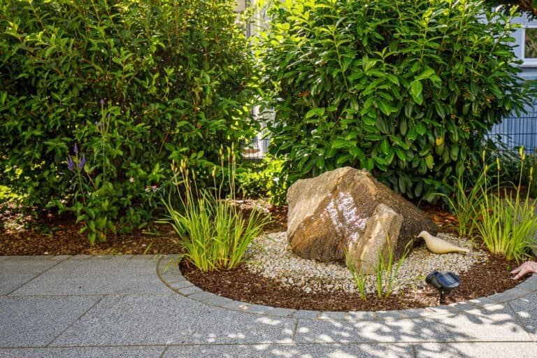Zierkiesbeet mit Quellstein und moderner Randbepflanzung entlang einer gepflasterten Terrasse als Teil einer hochwertigen Gartengestaltung in Bamberg von BELLA FLORA GmbH.