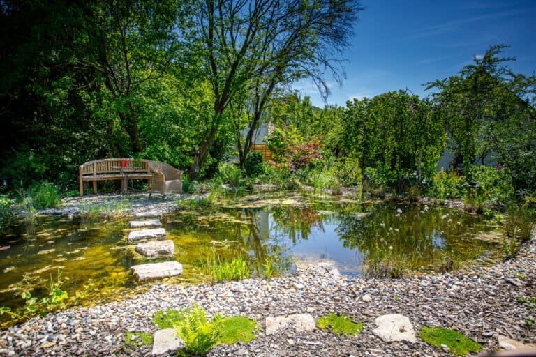 Großzügiger Naturteich mit geschwungenem Kiesufer, Naturstein-Trittplatten und integriertem Sitzplatz als Teichbau und Gartengestaltung in Fränkische Schweiz von BELLA FLORA GmbH.