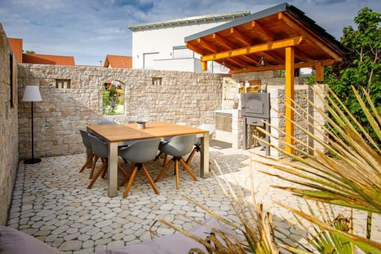 Modern gestalteter Sitzplatz mit Betonsteinmauer, Holzüberdachung und Outdoor-Küche als Terrassenbau in Bamberg von BELLA FLORA GmbH.