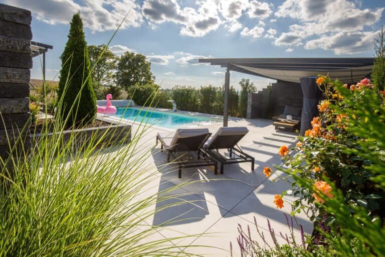 Moderne Poolterrasse mit Feinsteinzeugplatten, Pergola und Staudenbepflanzung im Privatgarten – Poolbau in Pretzfeld von BELLA FLORA GmbH.