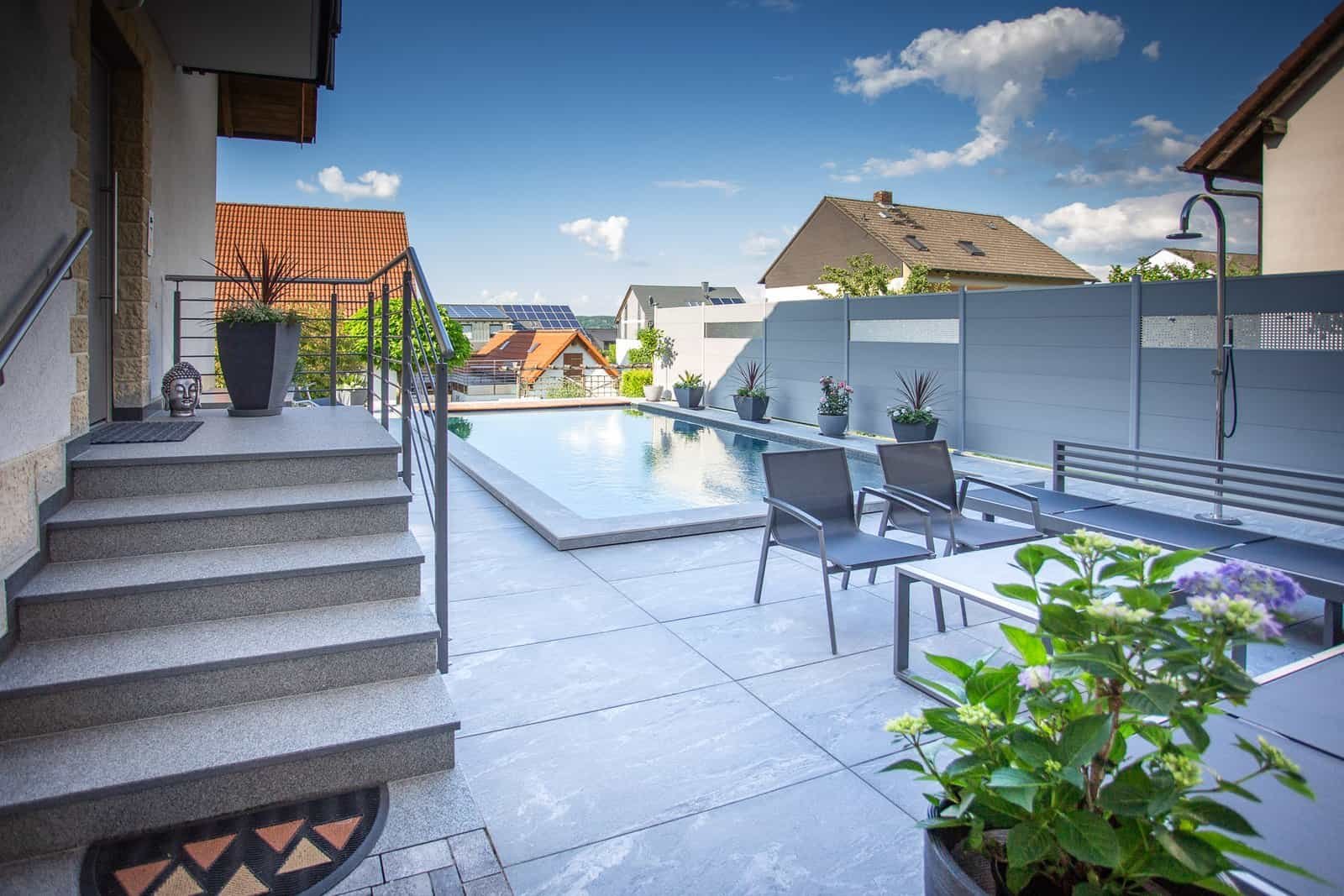 Moderne Poolanlage mit großformatigen Feinsteinzeugplatten und Sichtschutzzaun im Privatgarten – Poolbau in Fränkische Schweiz von BELLA FLORA GmbH.