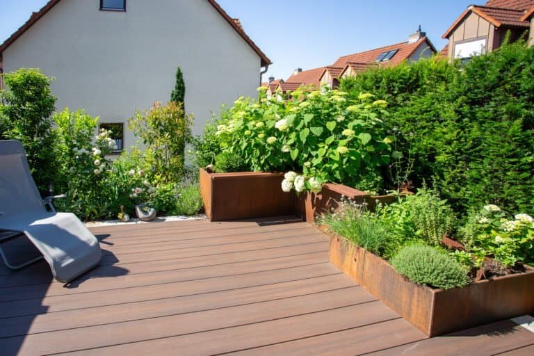 Moderne WPC-Terrasse mit Cortenstahl-Hochbeeten und Hortensienbepflanzung im Privatgarten – Terrassenbau in Bamberg von BELLA FLORA GmbH.