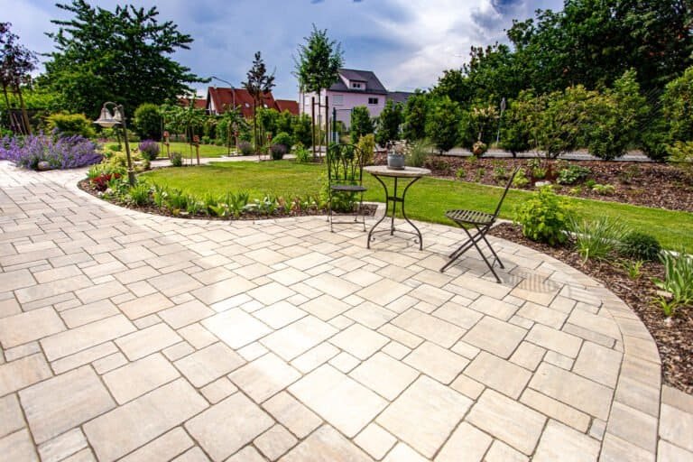 Großzügige Terrasse mit beigefarbenen Betonplatten und geschwungener Randeinfassung – Terrassenbau in Effeltrich von BELLA FLORA GmbH.
