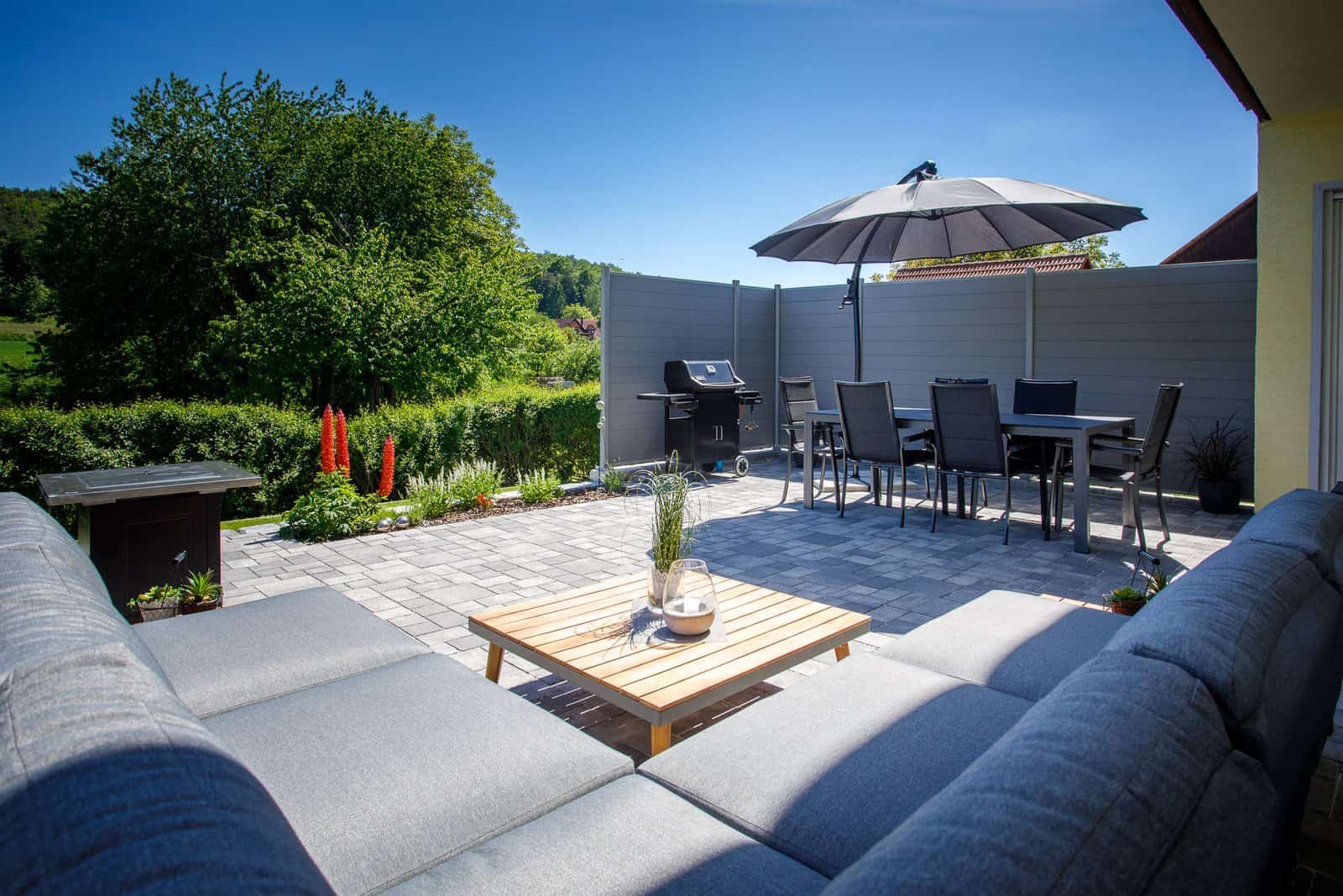 Modern gepflasterte Terrasse mit Sichtschutzzaun und Essbereich – Terrassenbau in Wiesenthau von BELLA FLORA GmbH.