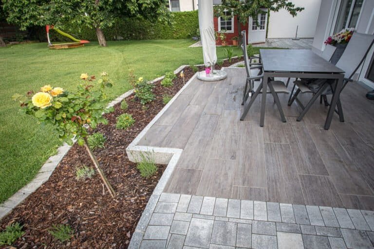 Keramikplatten im Holzdesign mit Sitzgruppe und dichter Heckenbepflanzung als Sichtschutz – Terrassengestaltung in Pretzfeld von BELLA FLORA GmbH.