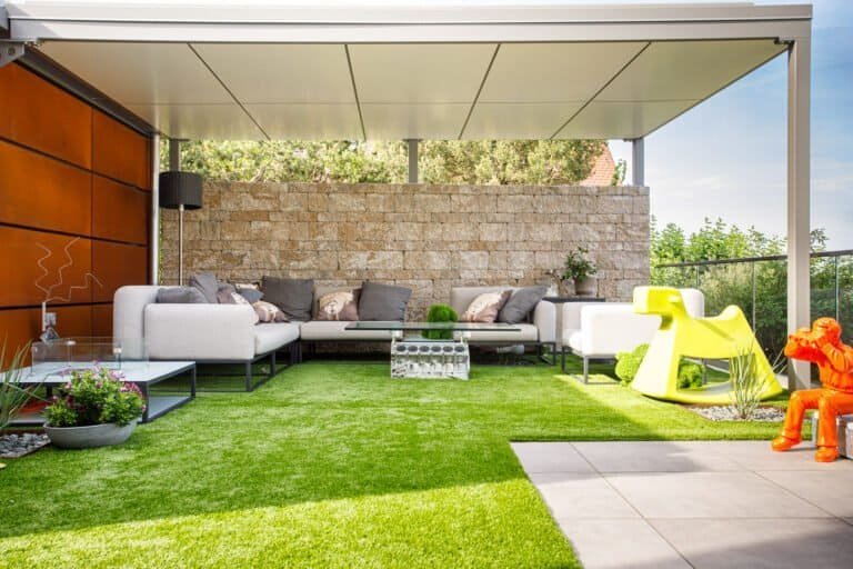 Überdachter Loungebereich mit Kunstrasen, Betonstein-Sichtschutzwand und Feinsteinzeugplatten – Terrassenbau in Ebermannstadt von BELLA FLORA GmbH.