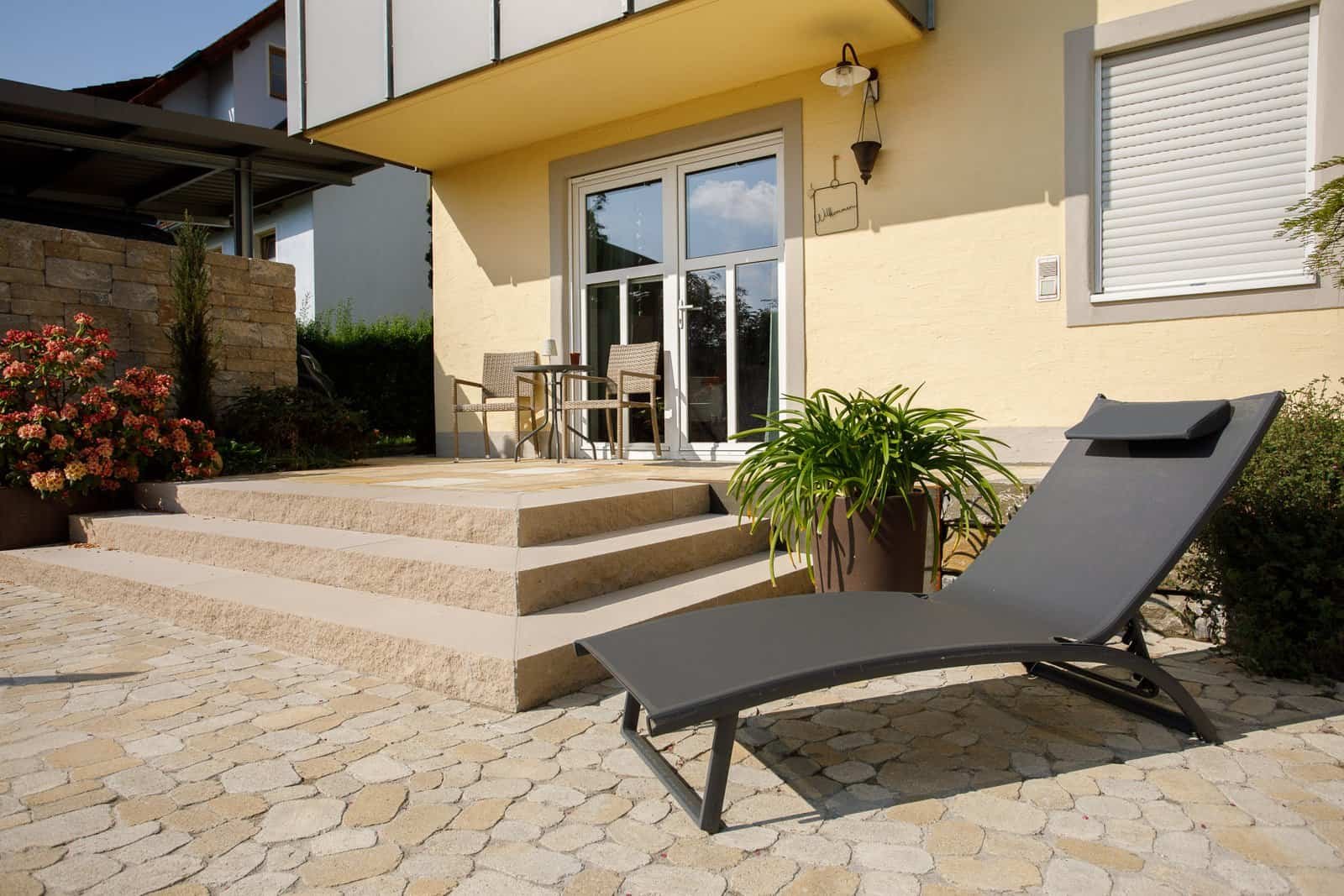 Terrasse mit Betonsteinstufen, Pflasterfläche und Hochbeet aus Mauersteinen am Wohnhaus – Terrassenbau in Ebermannstadt von BELLA FLORA GmbH.